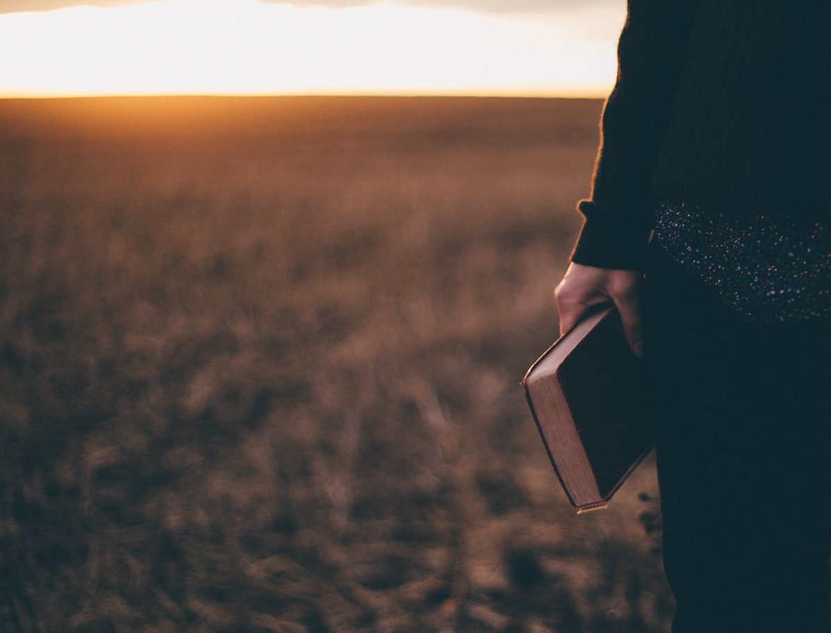 person holding book while standing on field